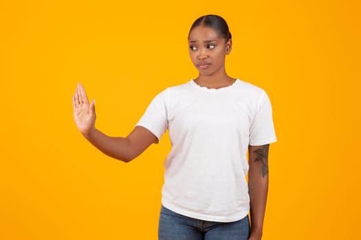 black woman makes stop gesture with hand on yellow background