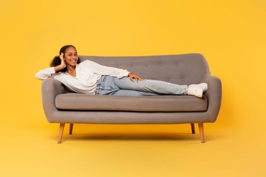 Black teenage girl relaxing resting on sofa over yellow background