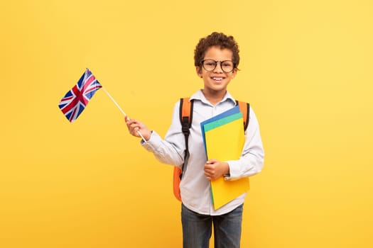 Happy schoolboy with UK flag and folders, bright yellow backdrop