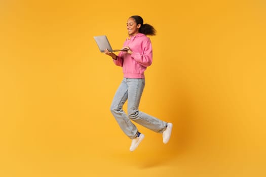 Carefree Black Teen Girl Holding Laptop Jumping Browsing Internet, Studio