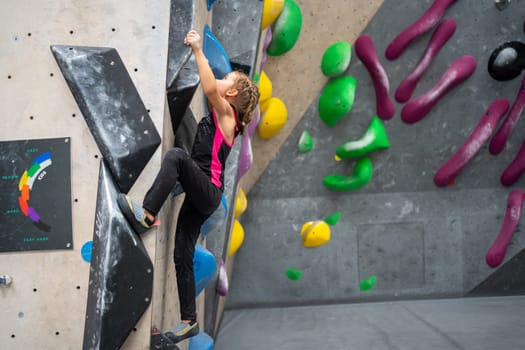Full length of sporty little girl in active wear climbing artificial wall. Female child practicing bouldering in sports center. Healthy lifestyle concept.