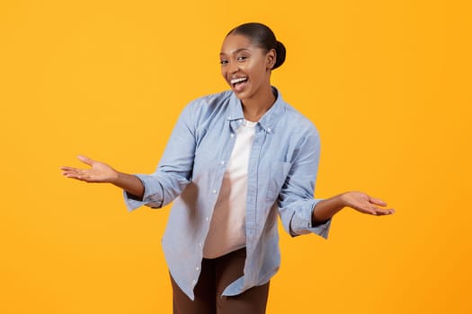 Toothy black lady in denim shirt gesturing against yellow backdrop