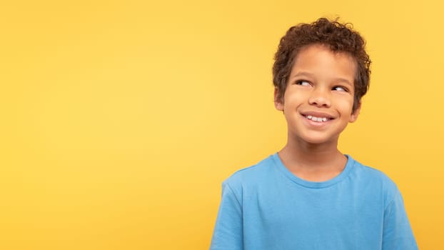 Thoughtful smiling boy looking up at free space on yellow background