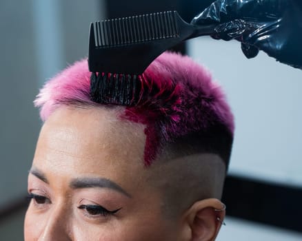 Close-up of the process. The hairdresser dyes the hair of an Asian woman in pink. Short extreme haircut.