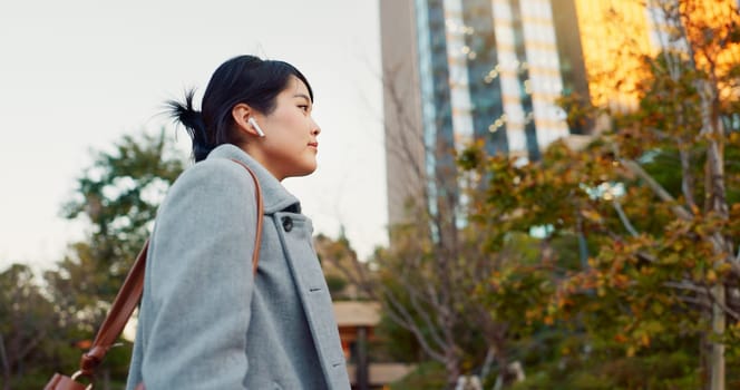 Woman, Asian and earphones, travel in city and commute to work with radio or podcast outdoor. Technology, spin and listening to music on journey, urban street and professional walking outdoor