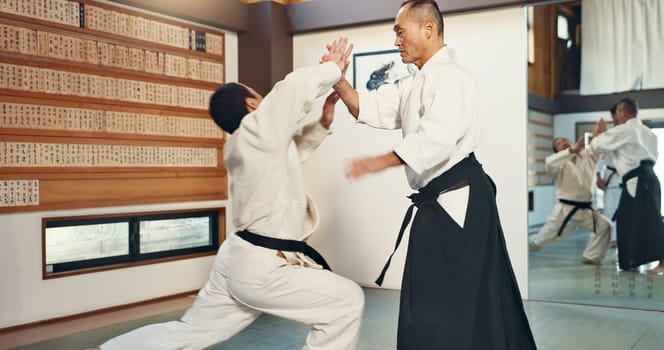 Aikido, sensei and master in a fight of martial arts with student in self defence, discipline and training. Demonstration, class or Japanese man with black belt in fighting with education of skill