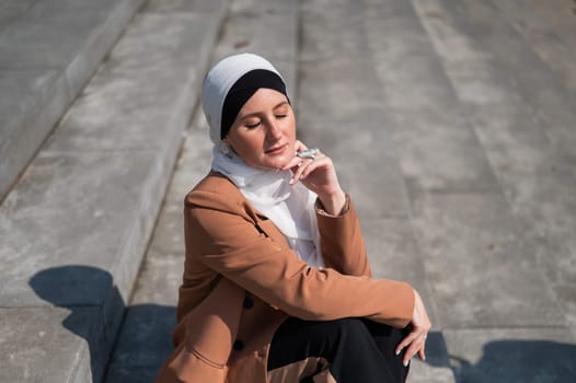 A young woman dressed in a hijab and a business suit is sitting on the stairs.