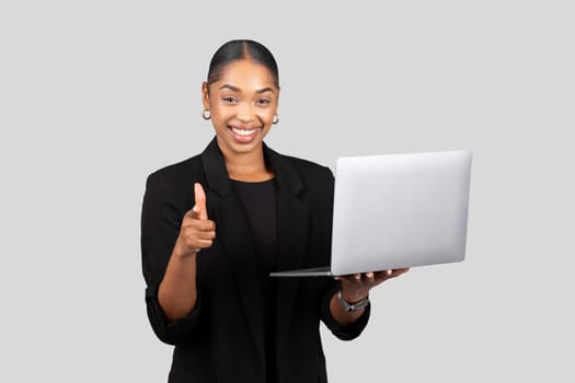 Enthusiastic young professional woman holding a laptop in one hand gives a thumbs up