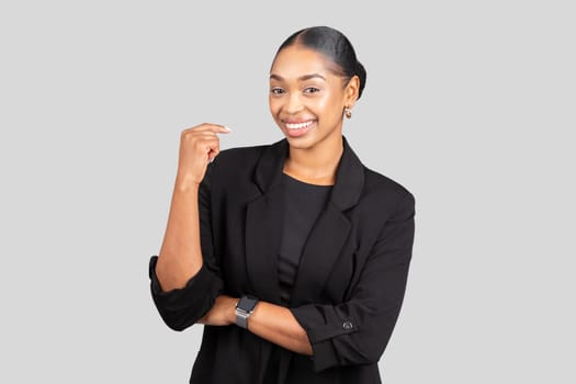 Joyful young woman in a black blazer, smartwatch on wrist, making a strong gesture with a smile