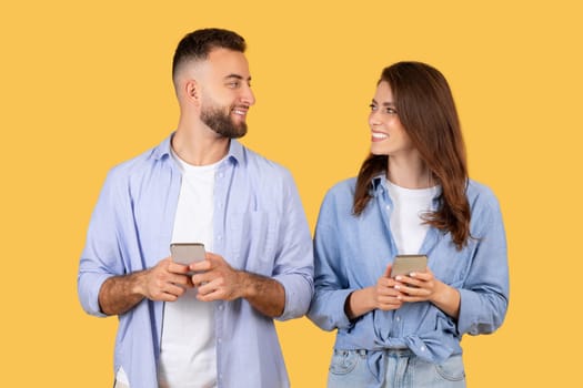 Smiling couple with phones, sharing content on sunny yellow background