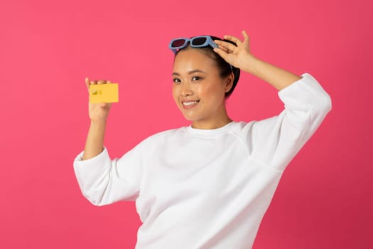 Trendy Shopping. Smiling asian woman with sunglasses on head showing credit card