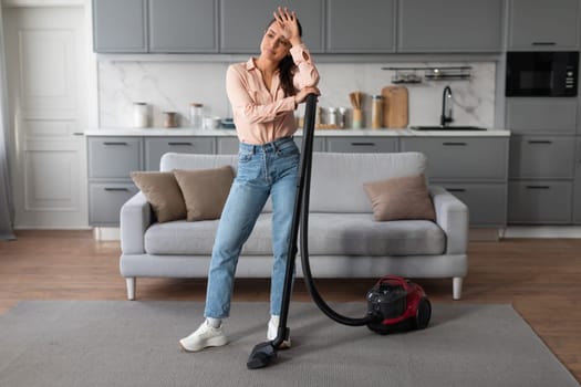 Tired woman pausing from vacuuming in modern room