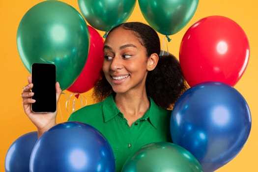 African teen girl presents blank smartphone screen among colorful balloons
