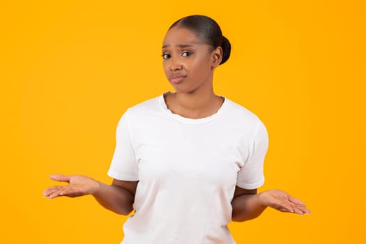 Portrait of Doubtful African American Lady Shrugging Shoulders, Yellow Background