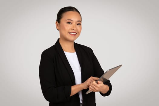 A cheerful Asian businesswoman uses a tablet with a focused expression