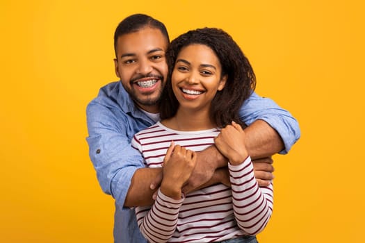 Loving black couple hugging with genuine smiles and looking at camera
