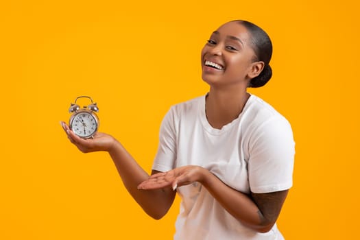 African American Lady Holding Alarm Clock On Yellow Studio Backdrop