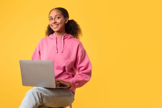 Black teen girl with computer learning sitting against yellow background