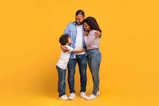 Little black boy embracing his parents while they standing on yellow background