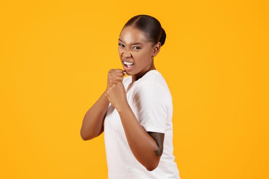 Determined black lady throwing punch at camera on yellow background