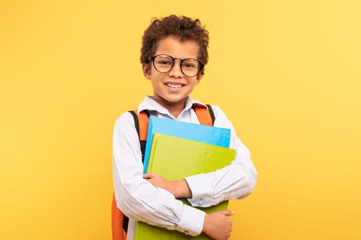 Smiling student with glasses and folders on yellow background