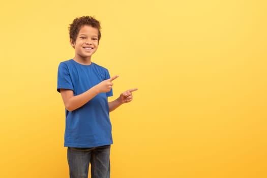 Boy pointing sideways at free space on yellow background