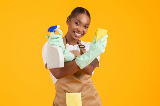 Happy african lady showing cleaning supplies holding detergent spray, studio