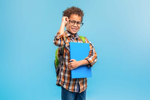 Smiling student in plaid, adjusting glasses, blue folder