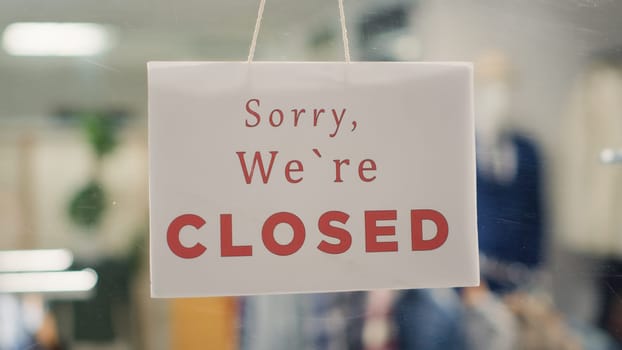 Extreme close up shot of message on designer clothing men premium showroom door announcing customers that shop is closed. Sorry we are closed sign in luxury fashion boutique with elegant clothes