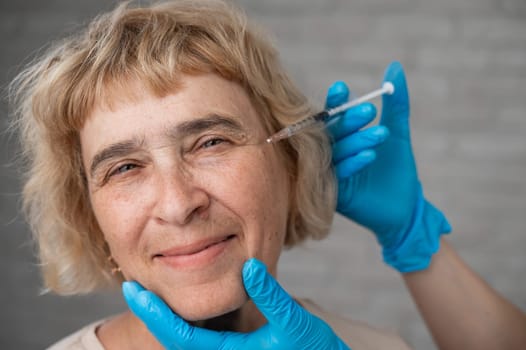 The doctor makes beauty injections in the face of an old caucasian woman. Wrinkles around the eyes.