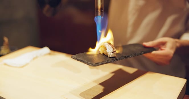 Hands, fire and cooking sushi with chef in restaurant for traditional Japanese food or cuisine closeup. Kitchen, flame for seafood preparation and person working with gourmet meal recipe ingredients.