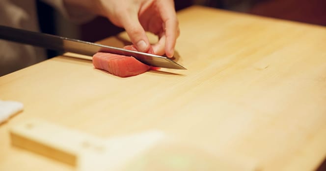 Hands, food and sushi chef cutting fish in restaurant for traditional Japanese cuisine or dish closeup. Kitchen, cooking on table for seafood preparation and person working with gourmet ingredients.