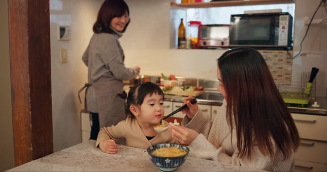 Family, Japanese and mother feeding daughter in kitchen of home for growth, health or nutrition. Food, girl eating ramen noodles in apartment with parent and grandparent for diet or child development