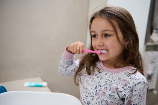 Caucasian child girl brushing her teeth in the bathroom. Oral care and dental hygiene to prevent caries and tooth decay