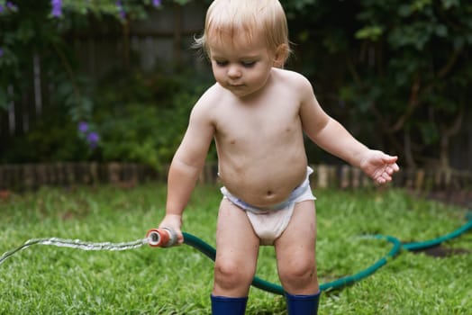Baby, playing with hose and garden, water and development with growth, curiosity and backyard. Toddler, child and infant in gardening, alone and childhood for skills, milestone and coordination