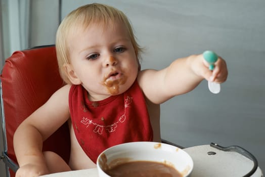 Feeding chair, eating and baby with spoon in a house for food, nutrition and fun while playing. Food, messy eater and boy kid at home with meal for child development, diet or nutrition while learning
