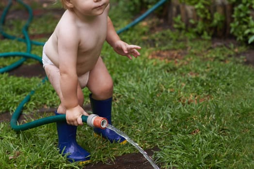 Baby, playing with hose and water, backyard and development with growth, curiosity and home. Toddler, child and infant in garden, alone and childhood for wellness, milestone and coordination