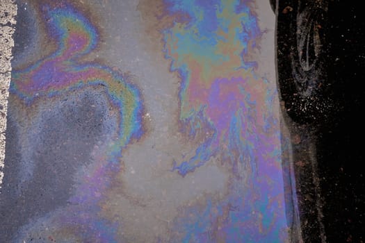 Spill of gasoline and oil on wet asphalt with reflection of car wheels