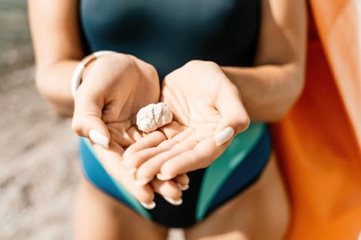 Beach vacation snapshot: A woman in a swimsuit holding a pebble in her hands, enjoying the serenity of the beach and the beauty of nature, creating a peaceful and relaxing atmosphere.