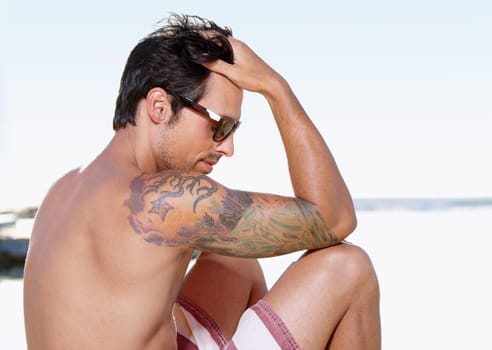 Swimsuit, sunglasses and beach with man, relax and summer with tropical island getaway and vacation. Person, holiday and guy with eyewear and travel with ocean, peaceful and tattoo with sunshine