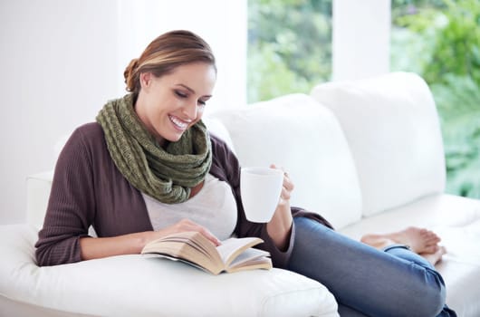 Happy, woman and reading book with coffee on sofa for story, novel or hobby in living room at home. Lady, fiction books and drinking cup of tea for literature, knowledge or comfortable break on couch