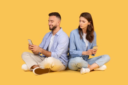 Man and woman sitting back-to-back, focused on their smartphones