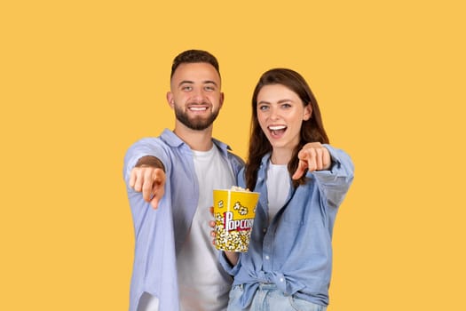 Excited couple pointing at camera with popcorn