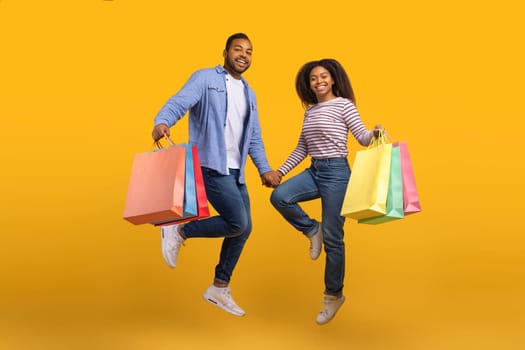 Cheerful Black Couple Holding Hands And Jumping With Shopping Bags