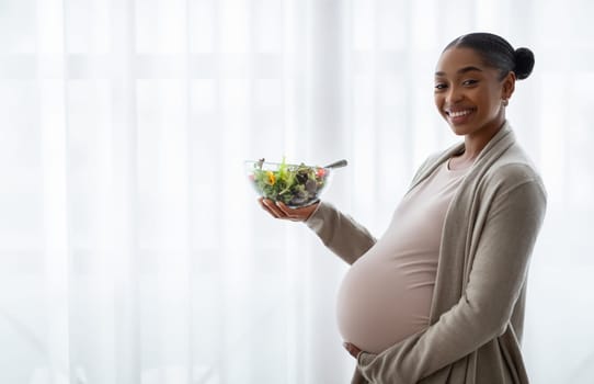 Happy young black lady expectant holding fresh vegetable salad