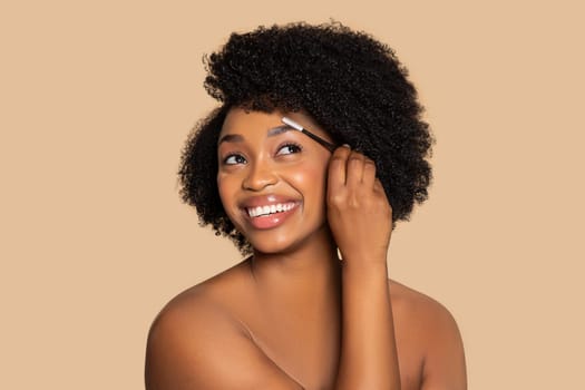 Happy woman grooming eyebrows with brush on beige backdrop