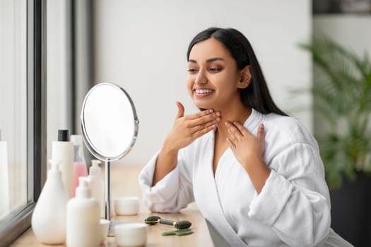 Positive millennial indian woman checking her neck in the mirror
