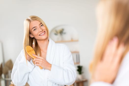 Blonde woman brushing hair for growth and strength in bathroom