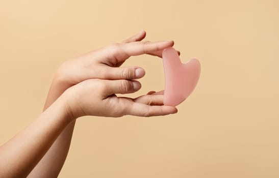 Hands elegantly display pink facial rose quartz gua sha tool at heart shape