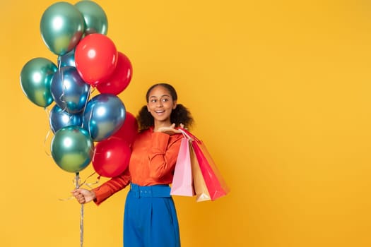 black teen shopper girl holding bright balloons and bags, studio